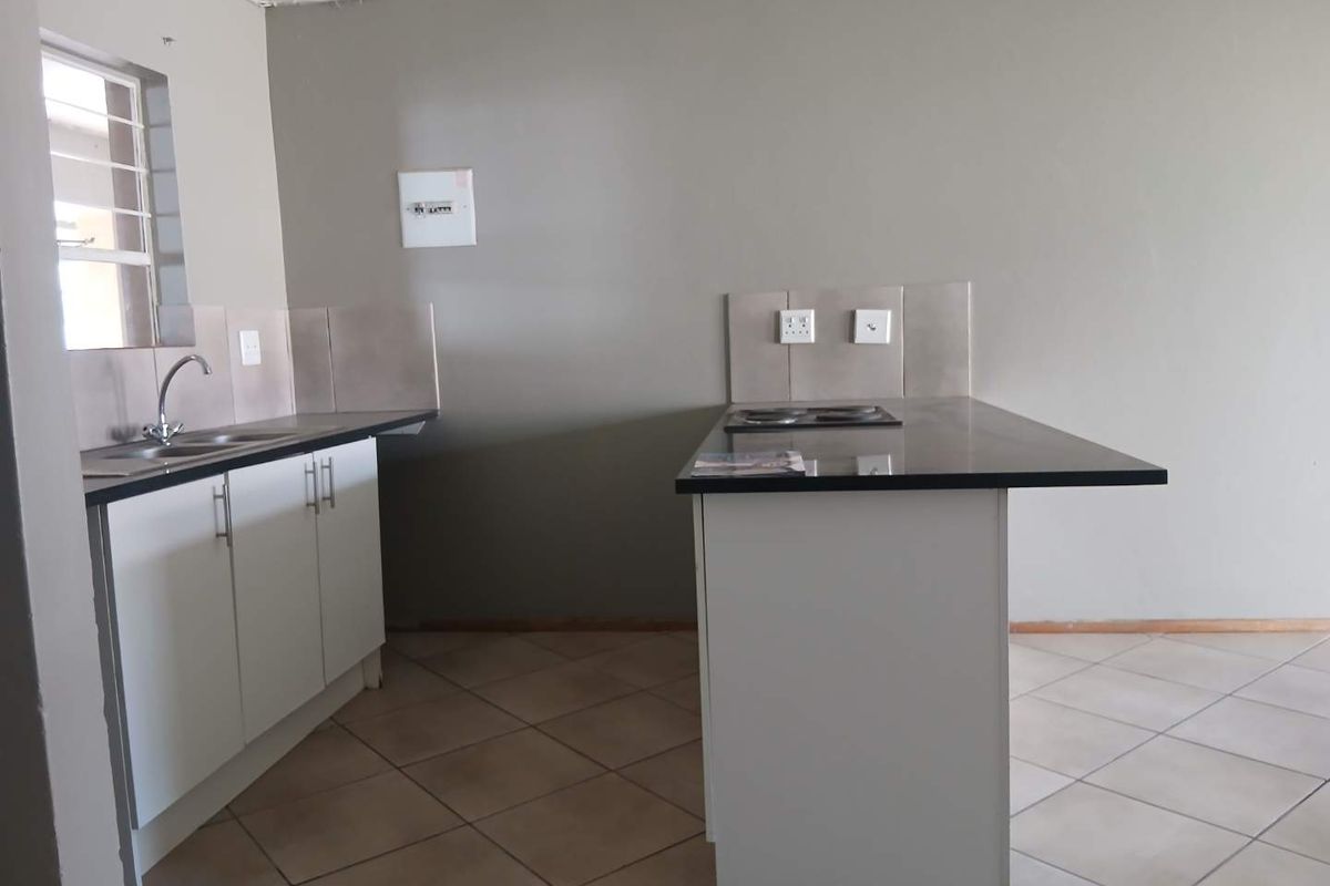 A functional kitchen featuring white cabinetry, dark laminate countertops, an integrated electric hob, and neutral tiled flooring in an open-plan layout.