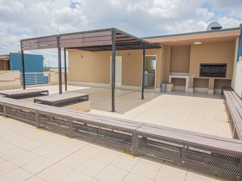 Spacious rooftop patio featuring a built-in braai, pergola structure, and tiled flooring, offering an ideal outdoor entertainment space.