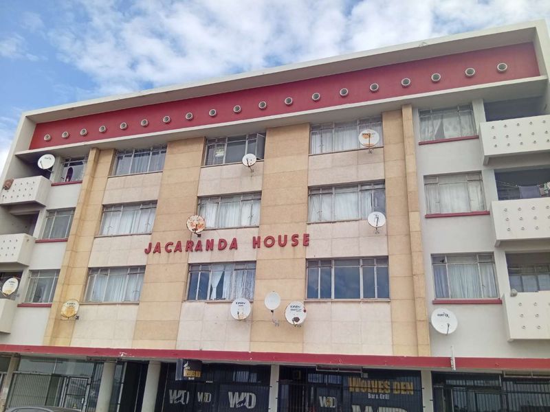 Exterior view of Jacaranda House, a multi-story apartment building featuring a prominent facade with ground-level commercial units and multiple satellite dish installations.