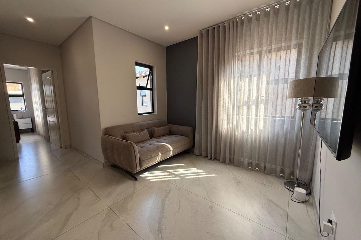 A modern living room featuring large format marble-look floor tiles, recessed downlighting, and a neutral color palette with a dark accent wall.