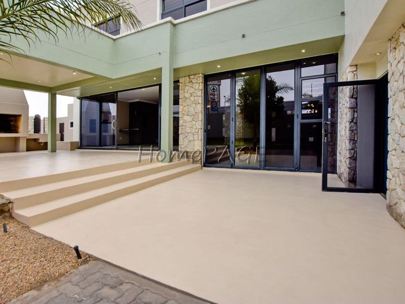 A spacious covered patio featuring stone cladding, a built-in braai, and large sliding glass doors providing seamless access to the interior living space.