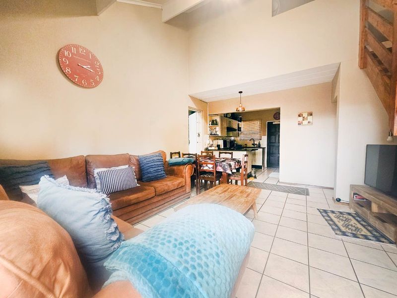 Open plan living area featuring tiled floors, a vaulted ceiling, and an adjoining kitchen space with a wooden staircase leading to the upper level.