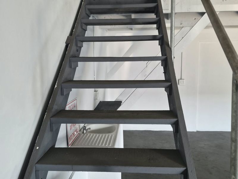 Industrial utility space featuring a metal staircase leading to a mezzanine level and a built-in utility sink.