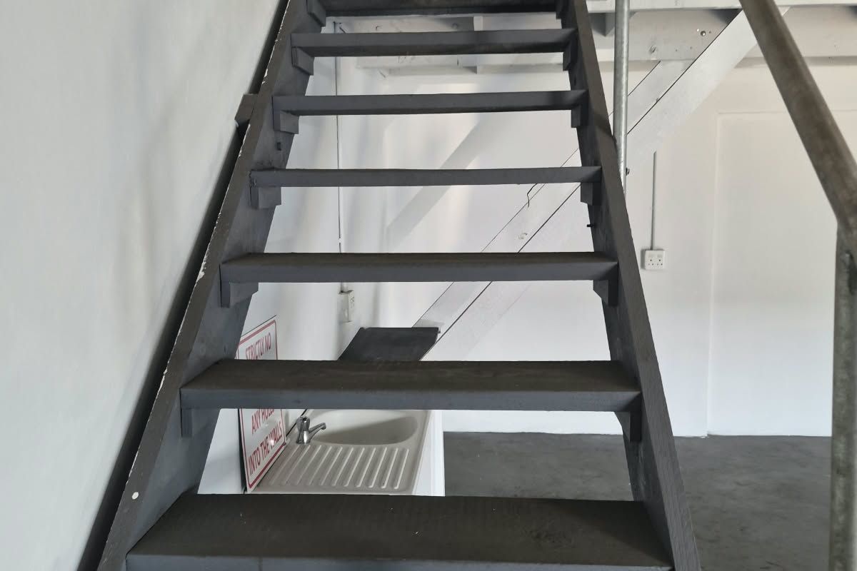 Industrial utility space featuring a metal staircase leading to a mezzanine level and a built-in utility sink.