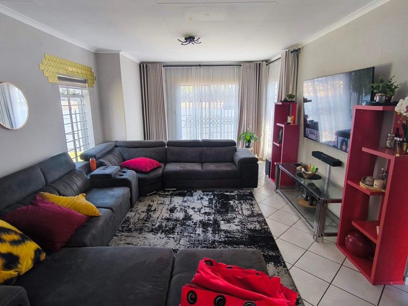 A comfortable living room featuring tiled flooring and a large sliding glass door with security gate, providing access to the outdoor area.