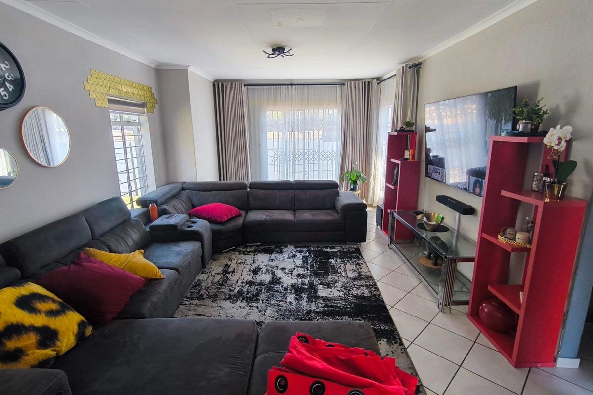 A comfortable living room featuring tiled flooring and a large sliding glass door with security gate, providing access to the outdoor area.