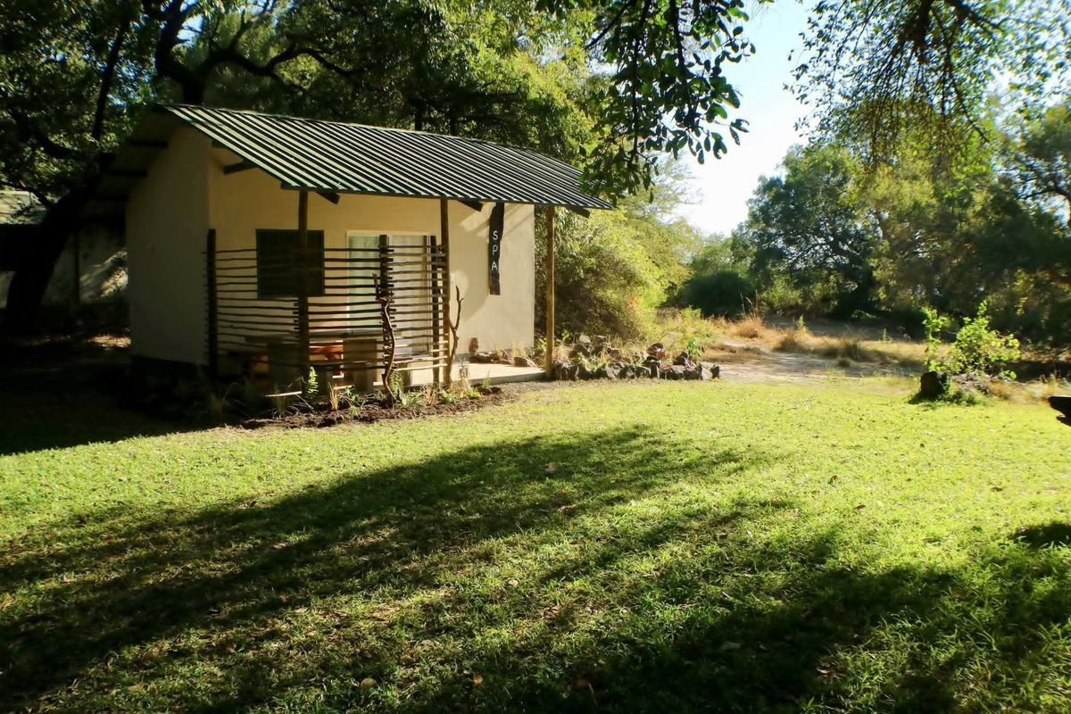 A detached spa building featuring a corrugated metal roof, timber support posts, and a private patio area set within a lush garden.