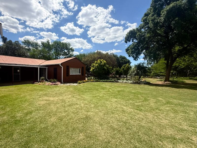 A spacious rear garden featuring a well-maintained lawn, mature trees, and a view of the property's exterior with a covered patio area.