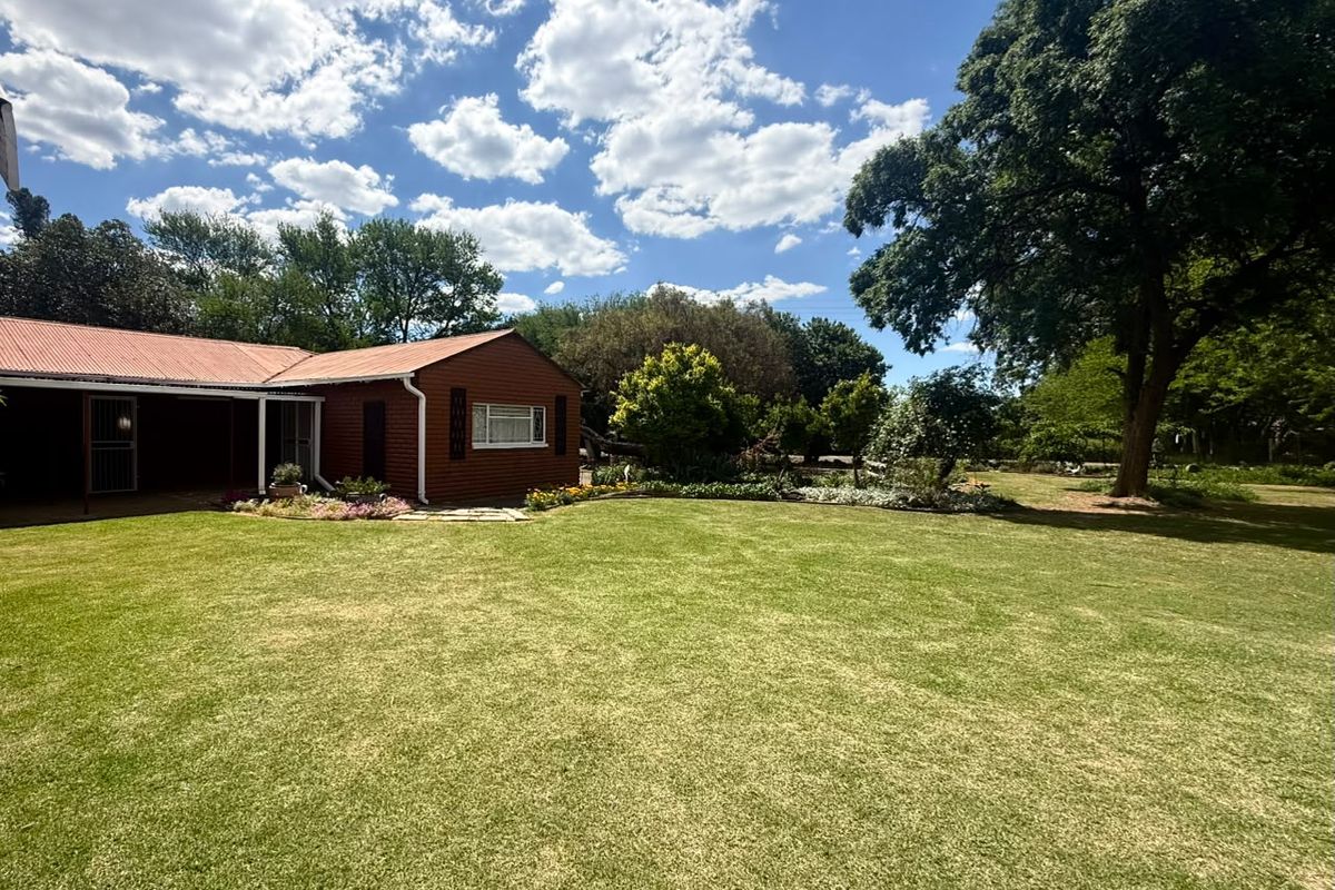 A spacious rear garden featuring a well-maintained lawn, mature trees, and a view of the property's exterior with a covered patio area.