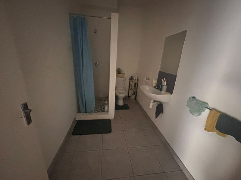 A functional bathroom featuring a shower enclosure, wall-mounted basin, and toilet with neutral floor tiling.