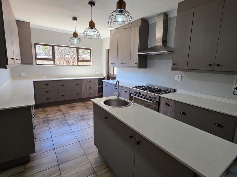Modern kitchen featuring neutral-toned cabinetry, stone countertops, a gas hob with extractor, and tiled flooring in an open, well-lit layout.