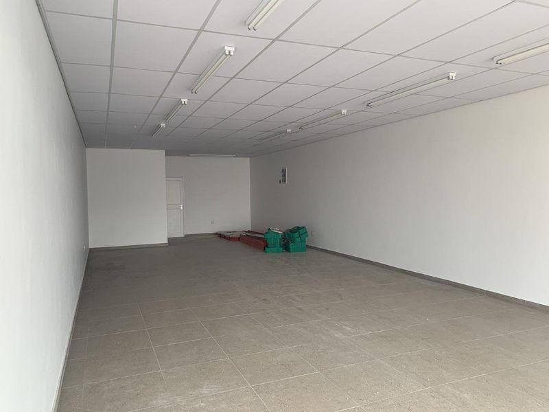 A vacant open-plan retail space featuring neutral tiled flooring, a suspended ceiling with integrated lighting, and clean white walls.