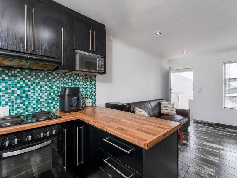 Open-plan kitchen and living area featuring modern black cabinetry, wooden countertops, a vibrant mosaic backsplash, and durable tiled flooring with direct outdoor access.