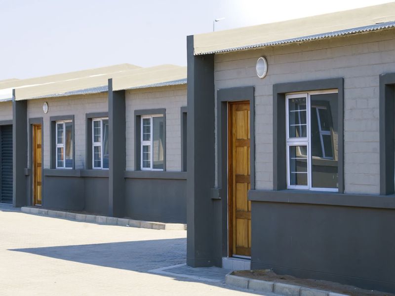 A row of modern townhouse units featuring grey brick facades, timber entrance doors, and paved driveway access.