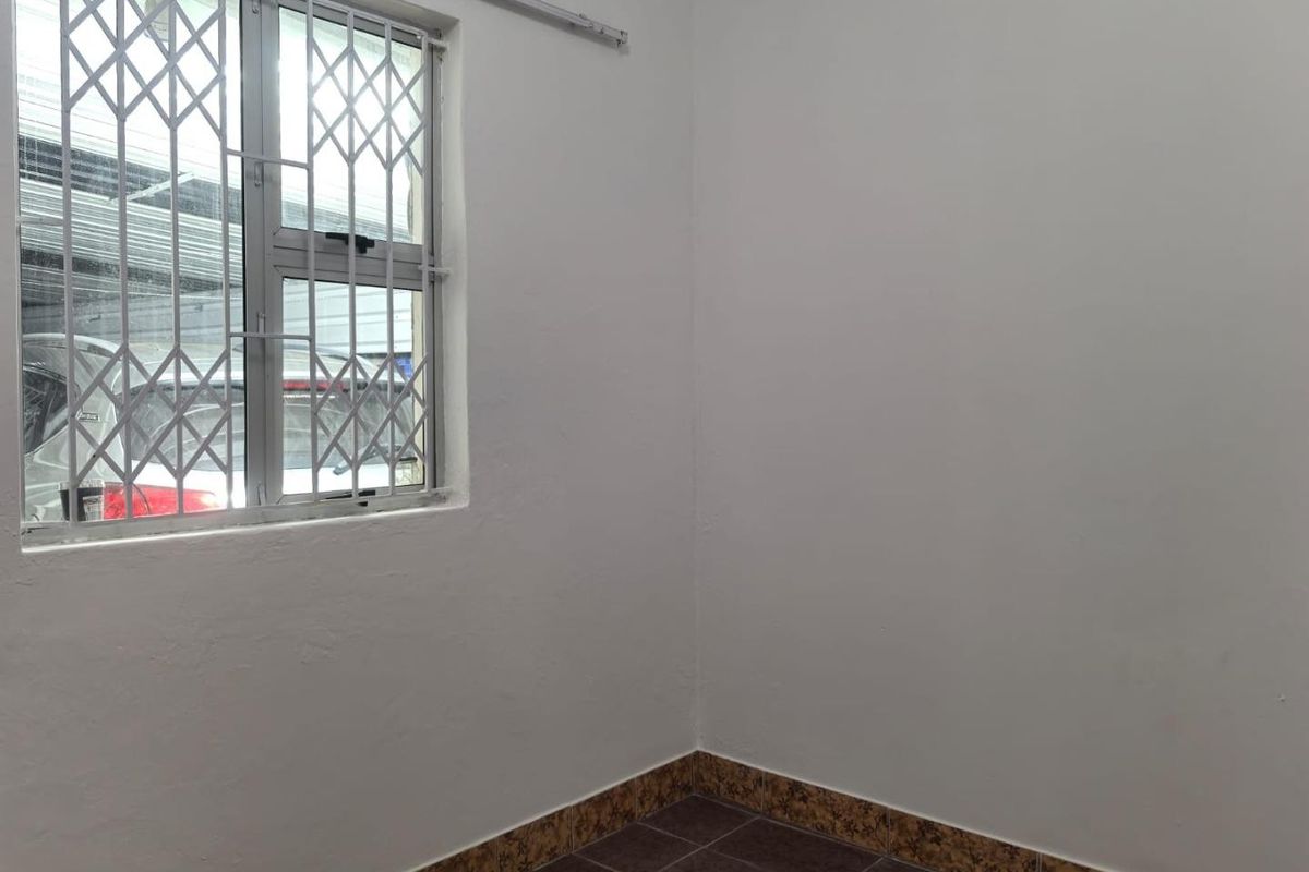 An empty bedroom featuring tiled flooring, white walls, and a window fitted with a security gate.