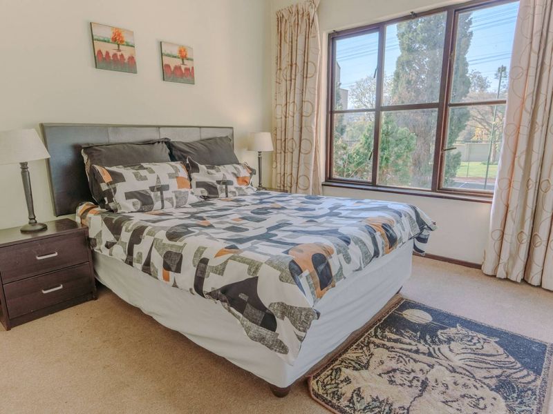 A well-lit bedroom featuring carpeted flooring and a large window providing natural light and exterior views.