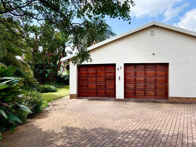 A double garage with wooden doors and a paved driveway, set against a landscaped garden.