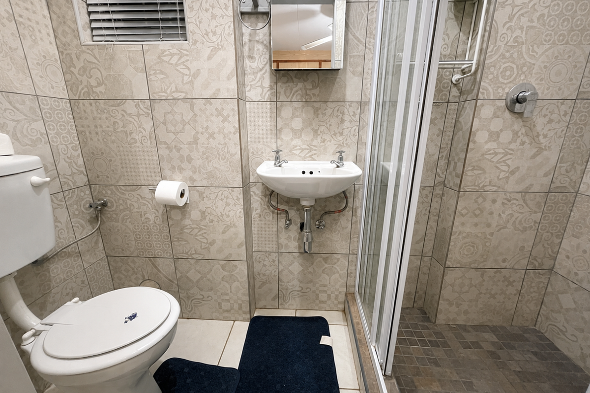 Compact bathroom featuring patterned wall tiles, a wall-mounted basin, a toilet, and a glass-enclosed shower cubicle.