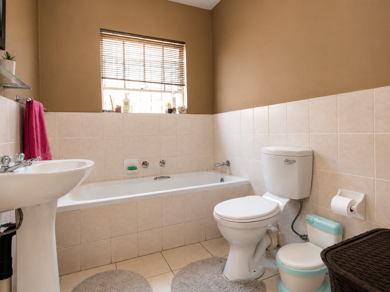 A functional bathroom featuring a pedestal basin, built-in bathtub, and toilet, finished with neutral wall and floor tiles.