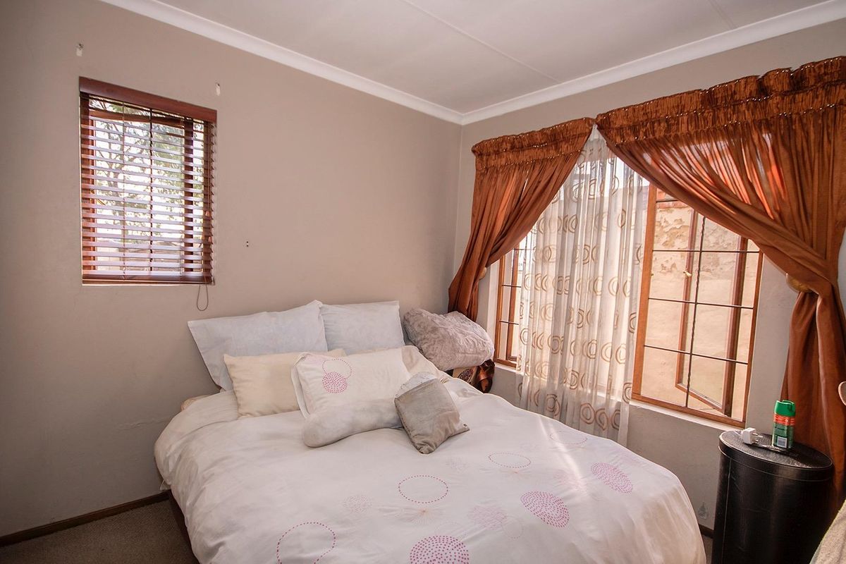 A bedroom featuring carpeted flooring, coving, and dual window treatments including wooden venetian blinds and curtains.