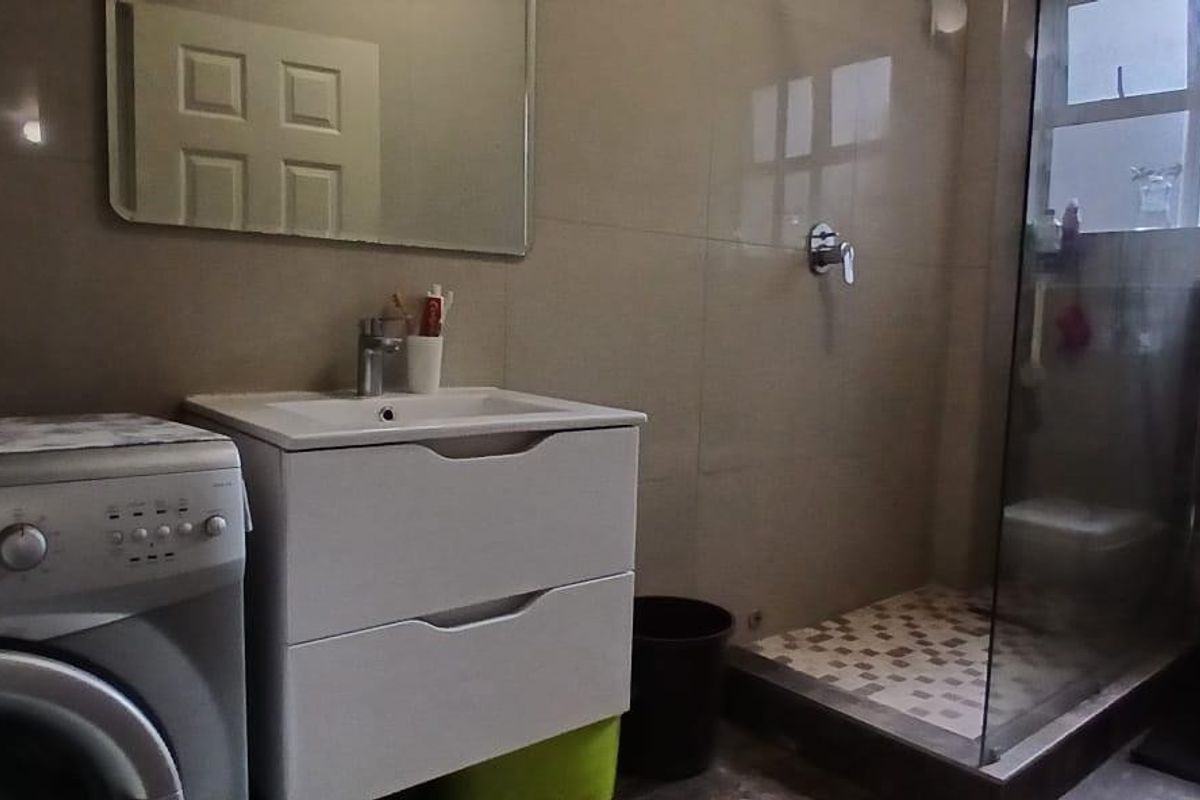 A functional bathroom featuring a vanity basin, glass-enclosed shower, and toilet, with neutral wall tiling and integrated laundry space.