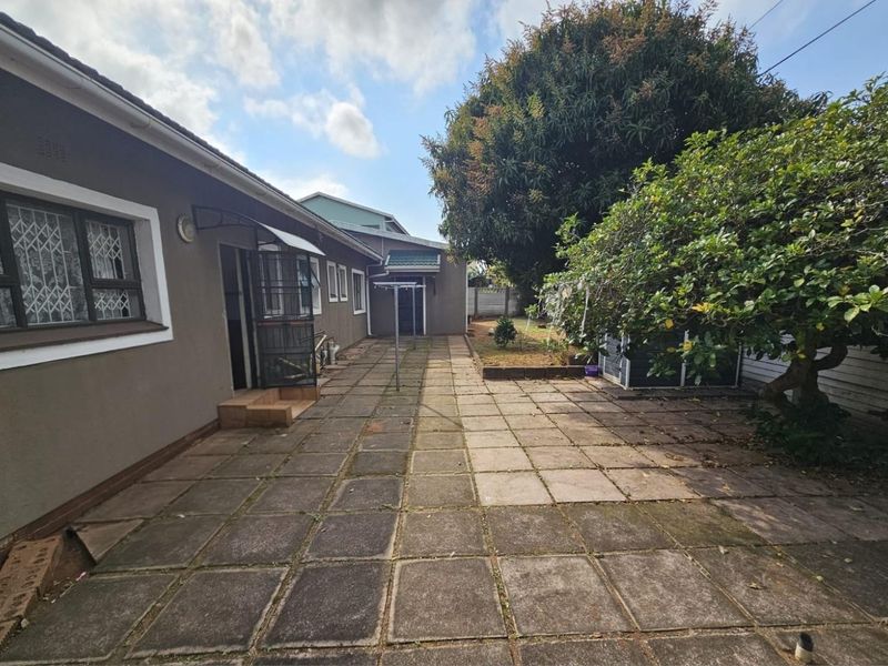 Rear exterior view of the property featuring a paved patio area, mature trees, and established garden space.