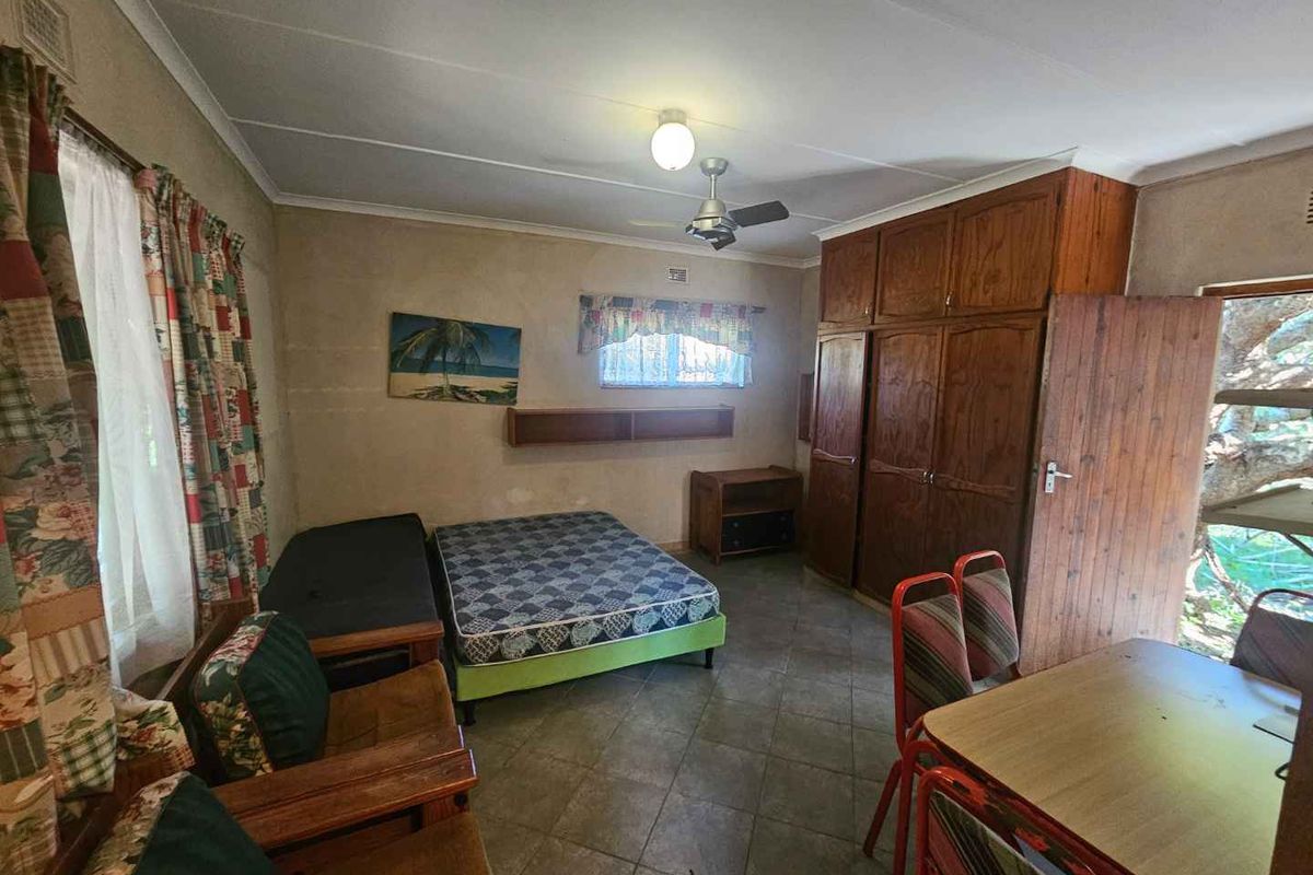 A bedroom featuring built-in wooden cupboards, tiled flooring, and a ceiling fan, offering a functional space with potential for modernization.