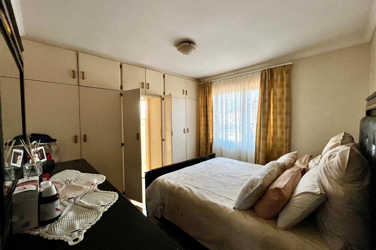 A bedroom featuring extensive built-in cupboards and natural light from a window, offering a functional space with potential for modern updates.