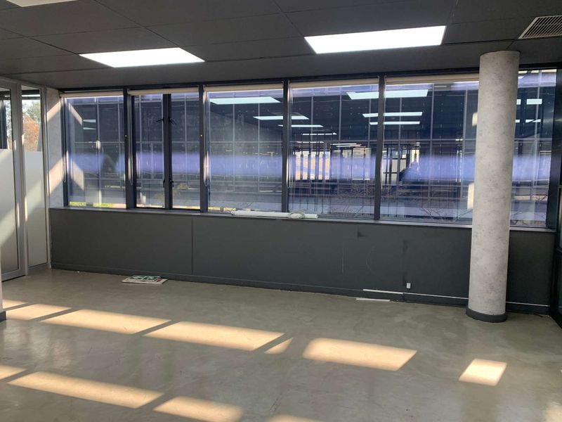 An empty office space featuring large windows, recessed ceiling lighting, a structural column, and polished concrete flooring.