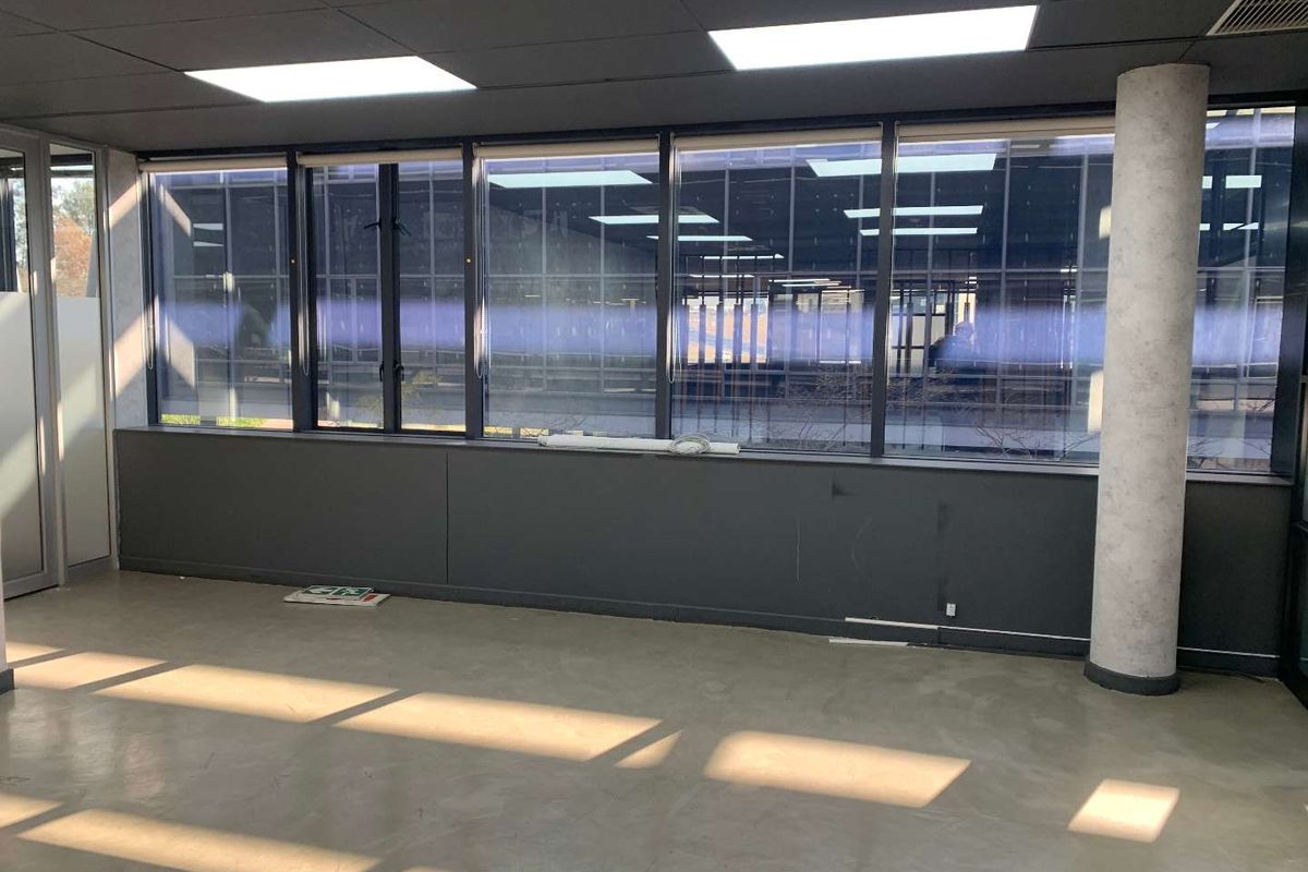 An empty office space featuring large windows, recessed ceiling lighting, a structural column, and polished concrete flooring.