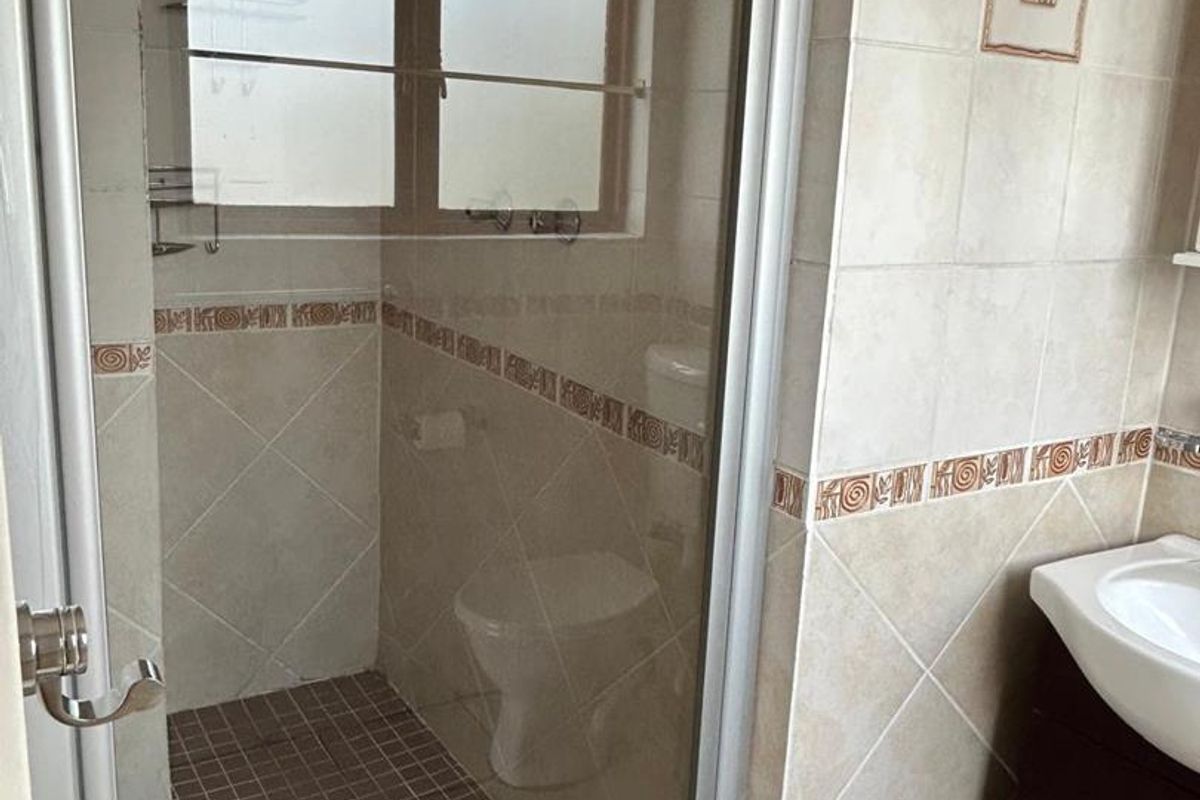 A functional bathroom featuring a glass-enclosed shower, a toilet, and a vanity cabinet with a wash basin, finished with neutral wall and floor tiles.