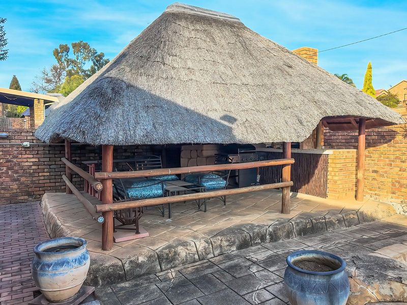 Outdoor thatched lapa area featuring a built-in braai, brick walling, and paved flooring, ideal for entertainment.