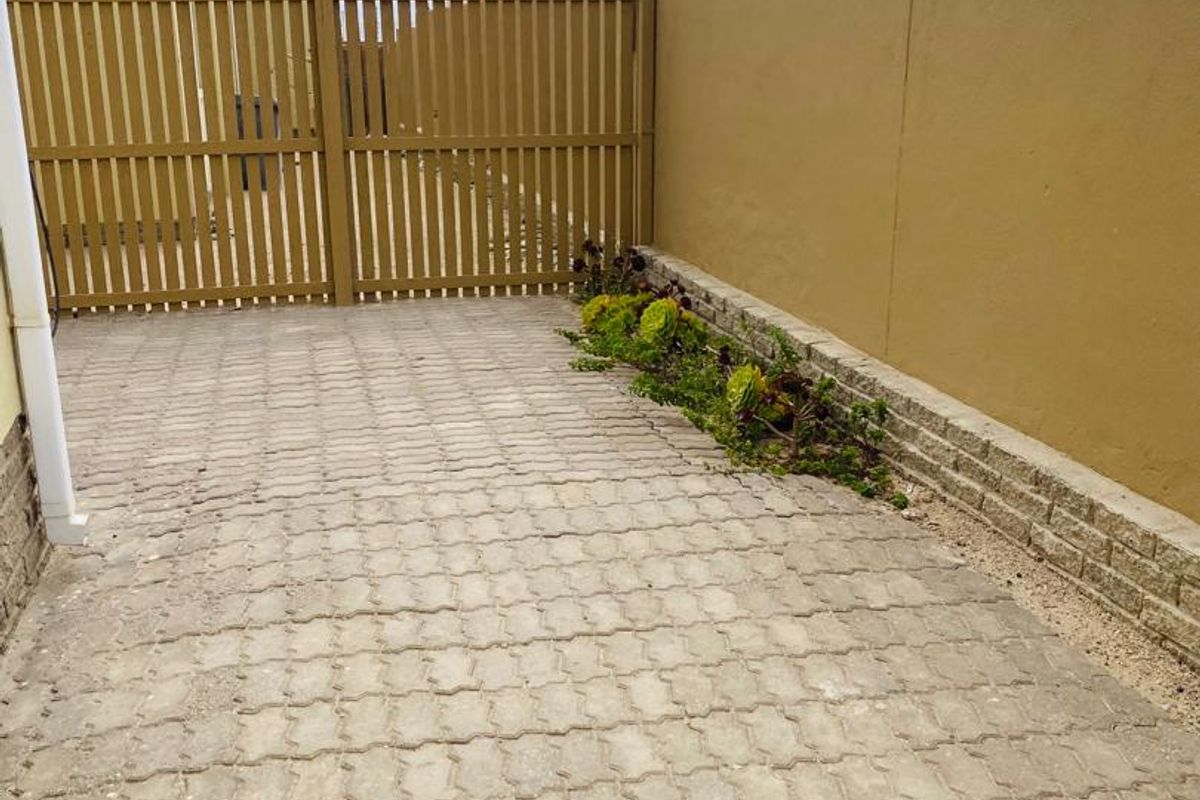 A paved rear courtyard area featuring a timber gate, boundary wall with electric fencing, and a small retaining wall with garden bed.