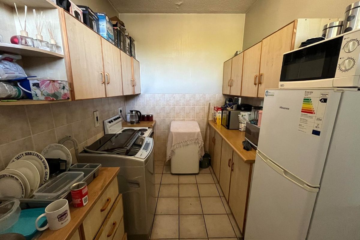 A functional galley-style kitchen featuring laminate cabinetry, tiled splashbacks, and tiled flooring, providing efficient workspace and storage.