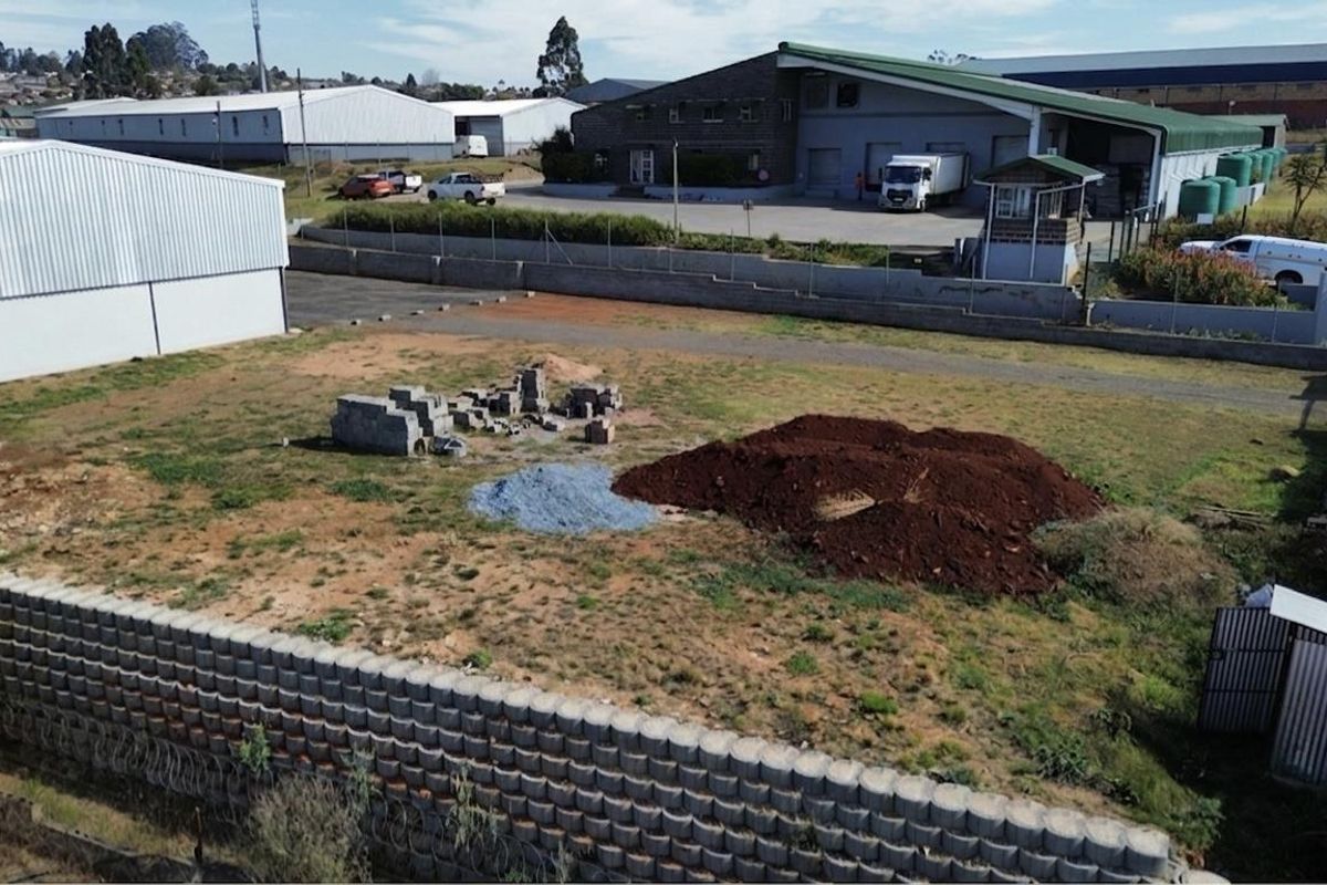 Aerial view of a vacant commercial land plot featuring perimeter retaining walls, security fencing, and existing paved access areas.