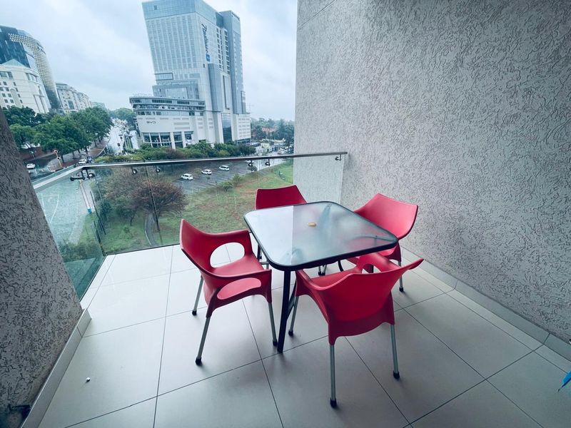 A modern balcony featuring tiled flooring, a sleek glass balustrade, and an elevated urban view of the surrounding city landscape.