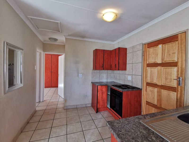A functional kitchen featuring built-in cabinetry, granite countertops, a built-in oven and hob, and tiled flooring, with an adjacent hallway leading to built-in storage.