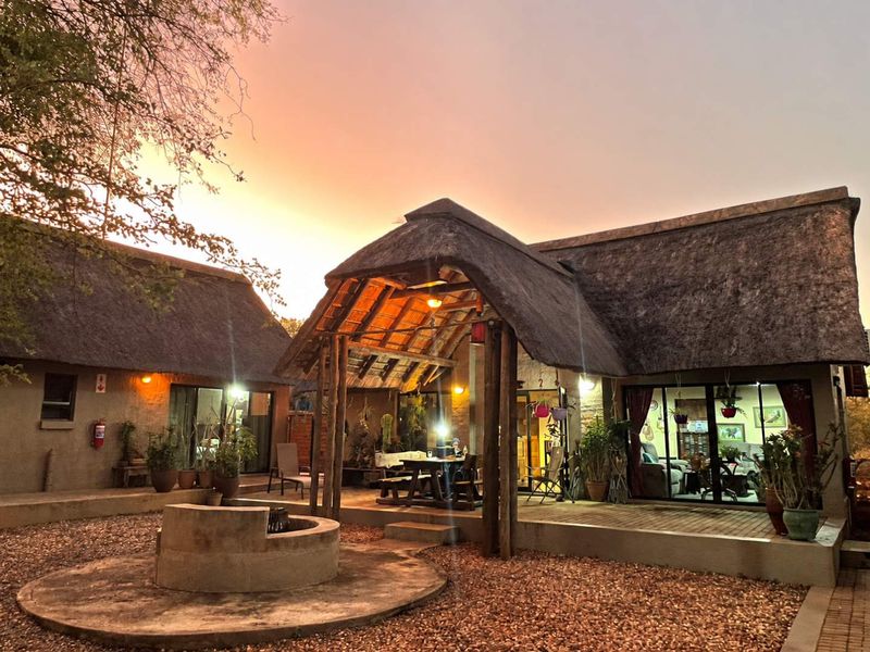 A charming thatched-roof residence featuring a spacious covered patio and a central built-in fire pit, perfect for outdoor entertaining in a serene setting.