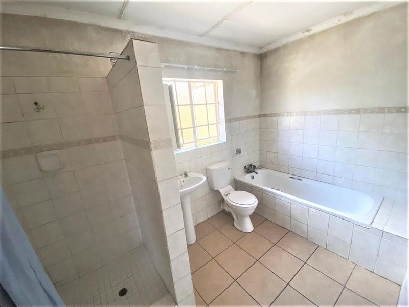 A spacious bathroom featuring a separate shower, bathtub, pedestal basin, and toilet, currently requiring cosmetic updates and finishing to the walls and ceiling.