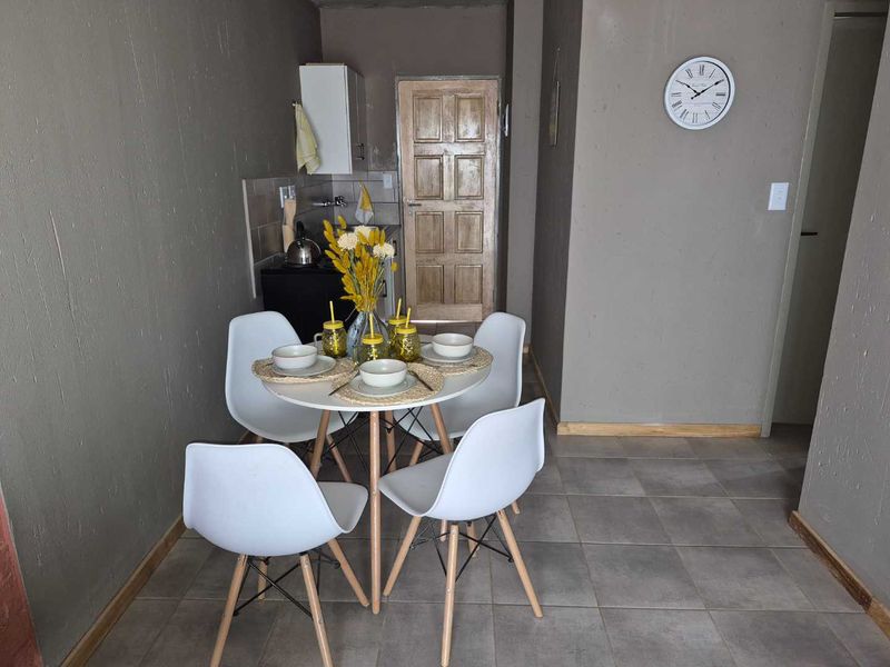 Open plan living and dining area featuring tiled flooring and a compact kitchen corner with built-in cabinetry and backsplash.