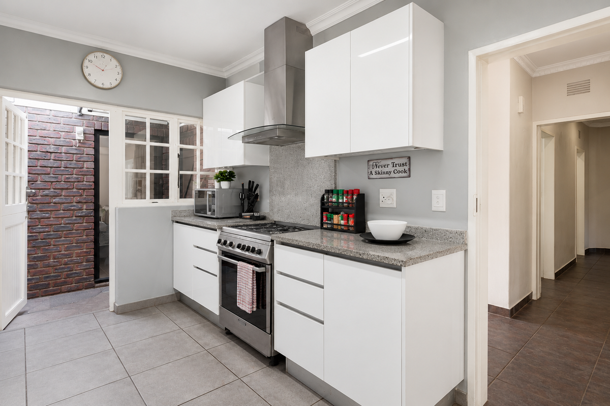 Modern kitchen featuring white gloss cabinetry, granite countertops, stainless steel gas stove with extractor fan, and direct access to an outdoor brick-walled courtyard.