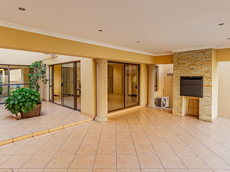 Spacious covered patio featuring tiled flooring, recessed lighting, and a built-in stone-clad fireplace, providing a seamless transition to the interior living spaces.