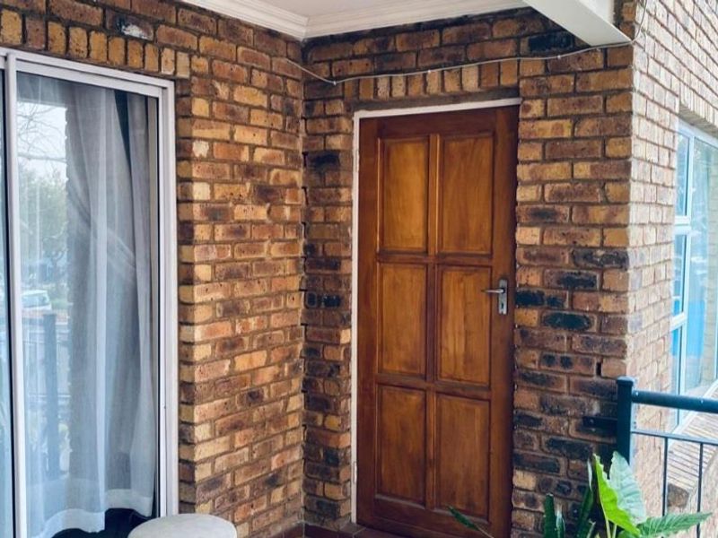 A balcony area featuring exposed brick walls, a timber entrance door, and a sliding glass door leading into the apartment.