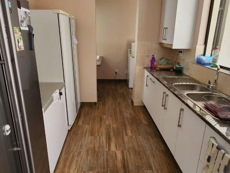 A functional kitchen featuring white cabinetry, granite countertops, a double sink, and wood-look floor tiles, leading into a secondary utility area.