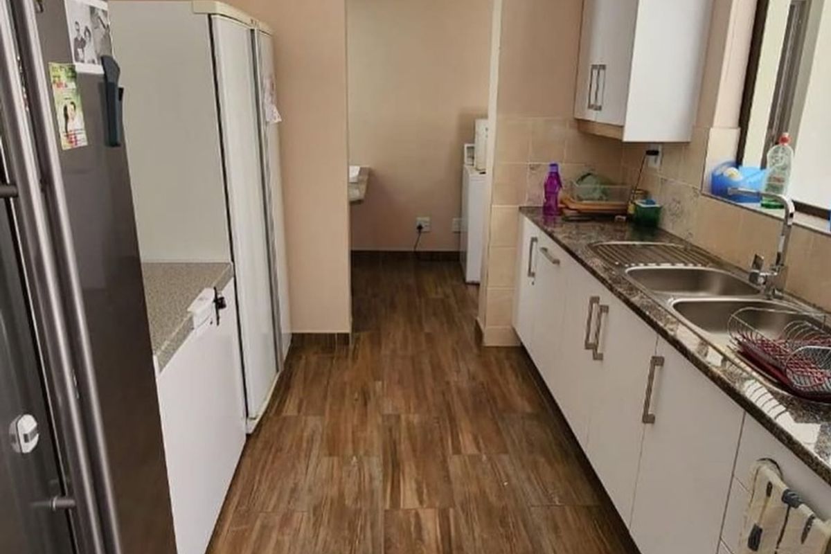 A functional kitchen featuring white cabinetry, granite countertops, a double sink, and wood-look floor tiles, leading into a secondary utility area.