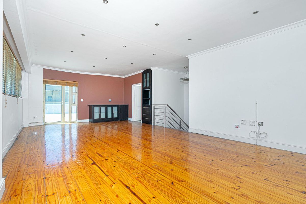 Spacious living area featuring polished timber flooring, recessed ceiling lighting, and a built-in display cabinet, with access to an outdoor balcony.