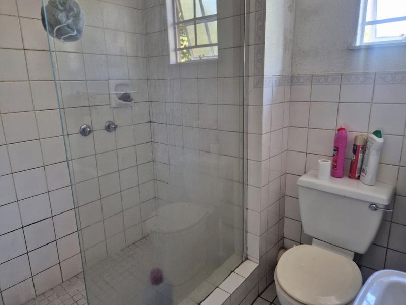 A functional bathroom featuring a glass-enclosed shower, ceramic tiling, and a standard toilet, requiring cosmetic updates to improve its overall condition.