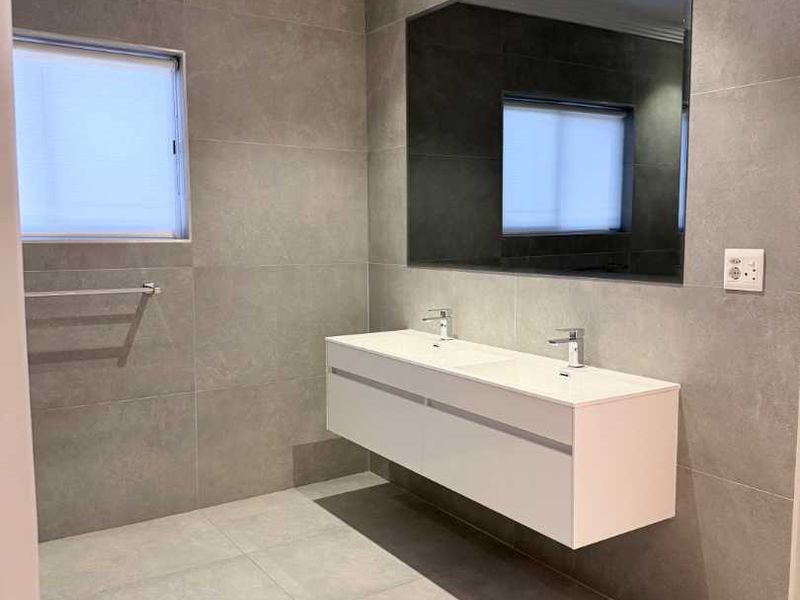Modern bathroom featuring a sleek floating double vanity, large wall-mounted mirror, and contemporary grey porcelain tiling throughout.