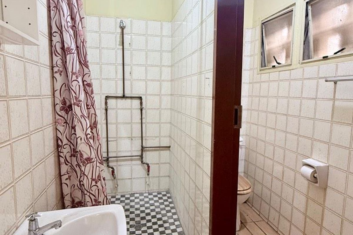 A functional bathroom featuring a pedestal basin, a shower with exposed plumbing, and a toilet, finished with dated wall and floor tiling.