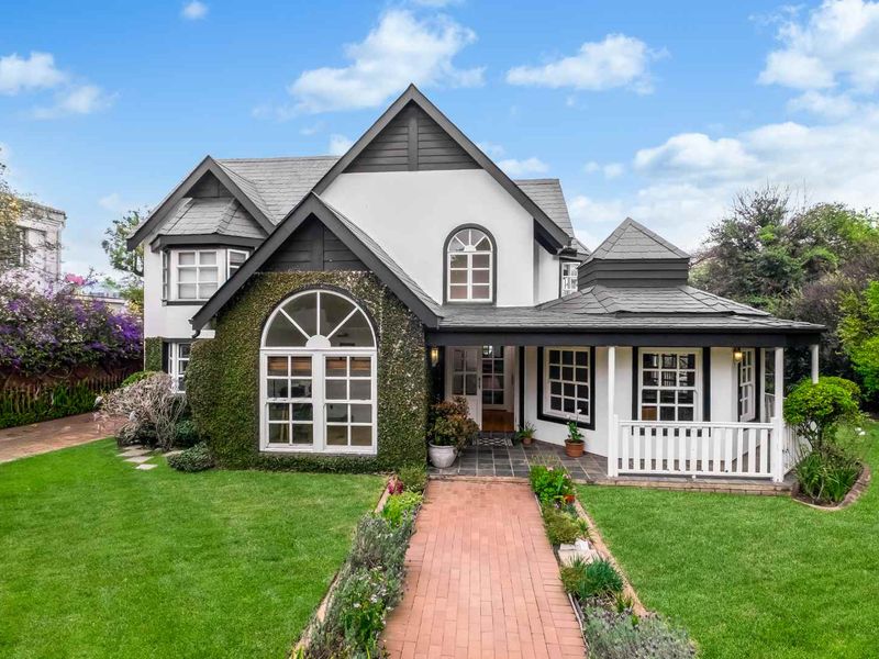 A charming double-story residence featuring a classic facade, slate roof, arched windows, and a welcoming brick pathway leading to a covered porch.